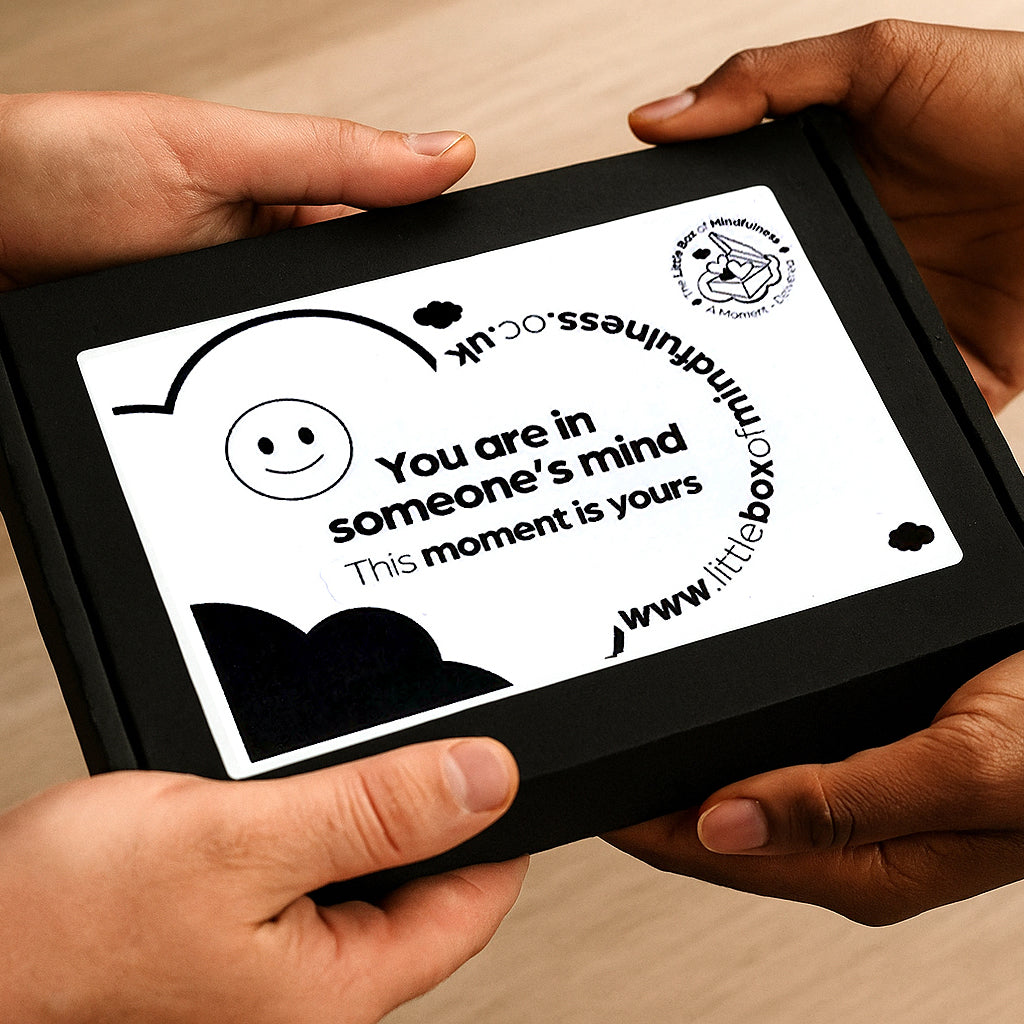 Two pairs of hands exchange a letterbox mental health gift. The words on the outside of the box reads - You are in someone's mind. This Moment is yours. 