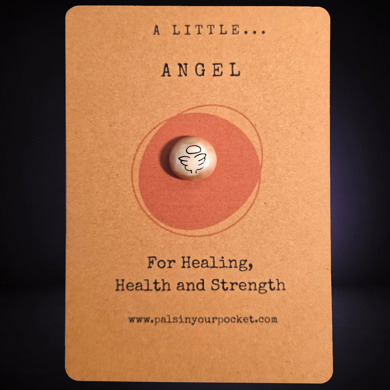 A pocket pal with angel illustration sits centered on a kraft paper backing card. The card has printed text reading 'A LITTLE ANGEL'