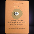 "A Little Calm” mindfulness card with a small white meditation pebble, featuring the message: “Strength exists when we quiet our mind. Be still. Restore."