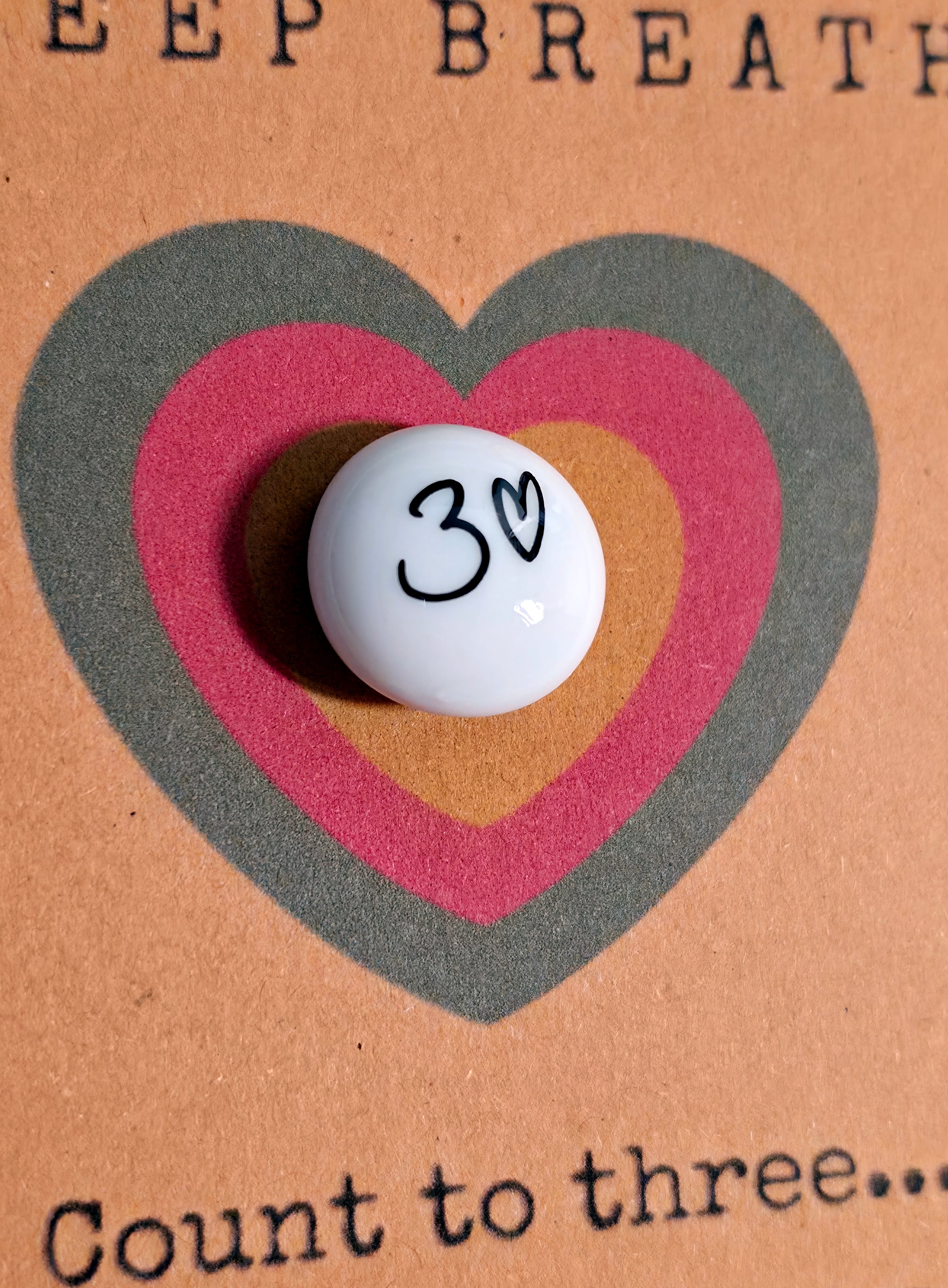 Close-up of Deep Breath mindfulness pebble with heart symbol on calming affirmation card about breathing and relaxation.