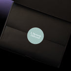 A close-up of a black gift box interior with a circular blue grey sticker in the centre that reads 'A Moment, Delivered' in white text.