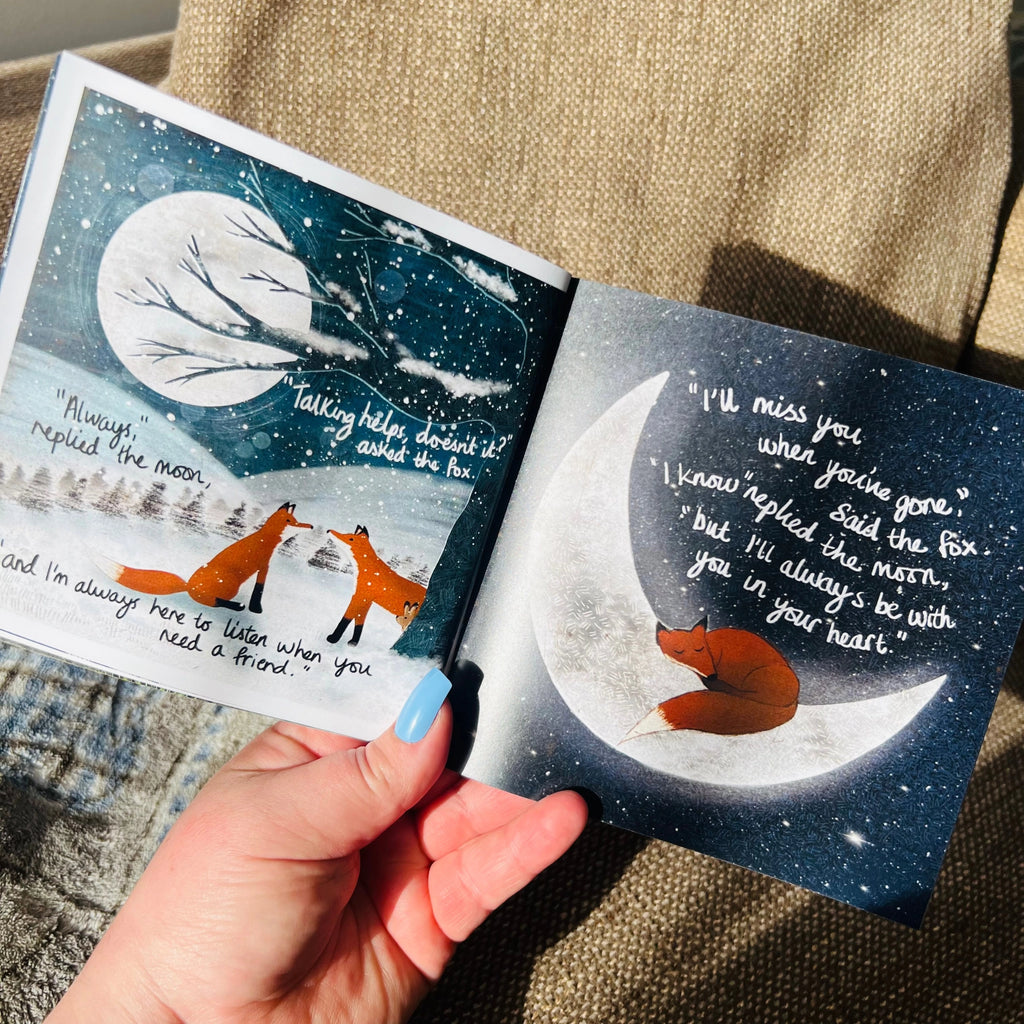 Open book with fox illustrations and moon on a textured surface