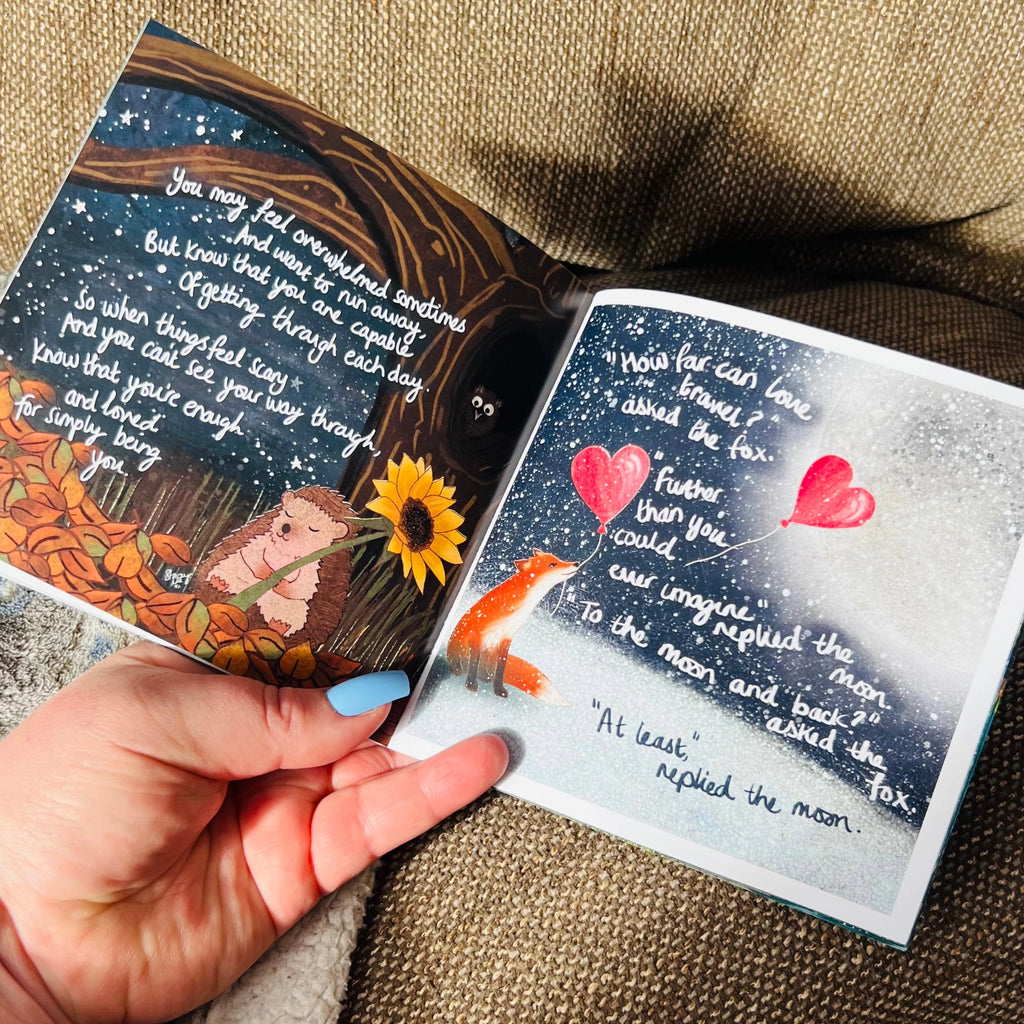 Open book with fox and hedgehog illustration held by a hand on a textured surface