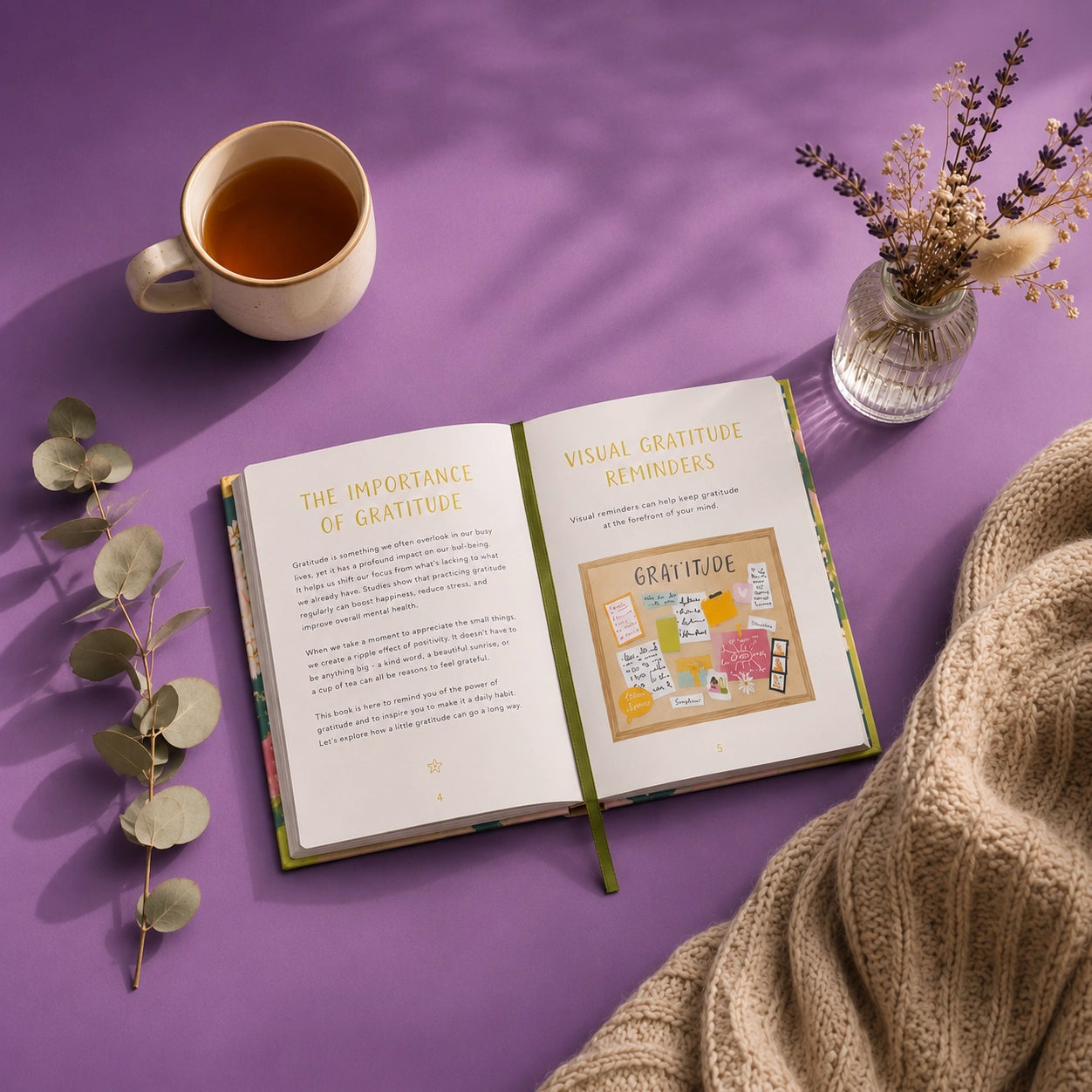 An open book titled 'The Importance of Gratitude' and 'Visual Gratitude Reminders' lies on a purple surface, styled with a cup of tea, dried flowers in a glass vase, eucalyptus leaves, and a beige knit blanket.