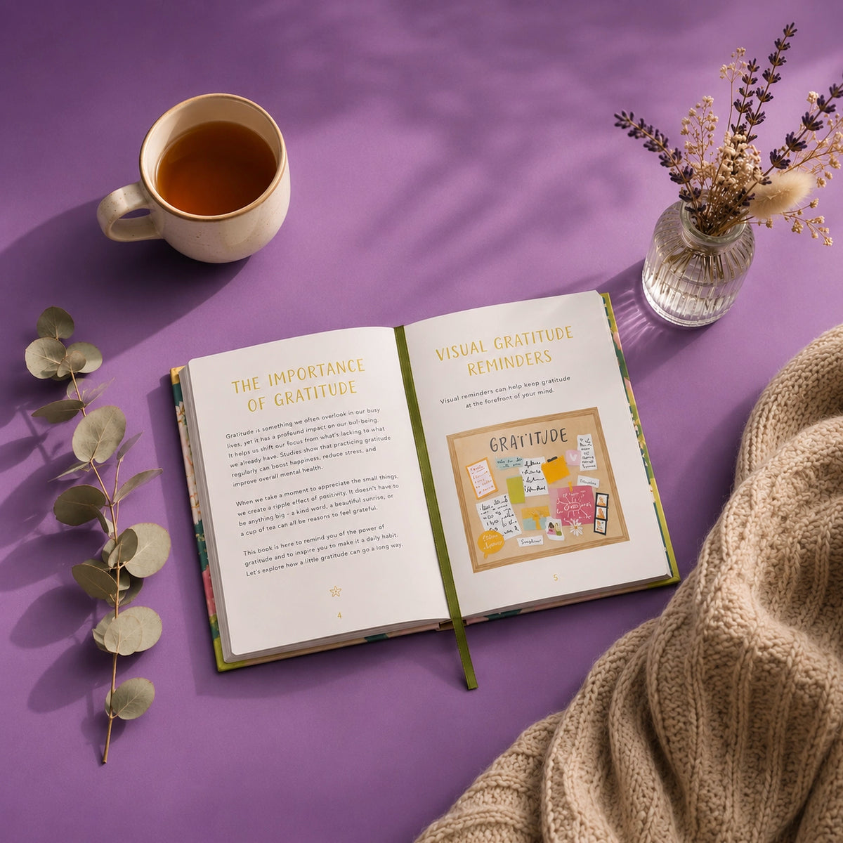 An open book titled 'The Importance of Gratitude' and 'Visual Gratitude Reminders' lies on a purple surface, styled with a cup of tea, dried flowers in a glass vase, eucalyptus leaves, and a beige knit blanket.