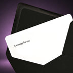 A white greeting card with the printed text 'A message for you' in black, partially tucked inside a black envelope against a dark purple background.