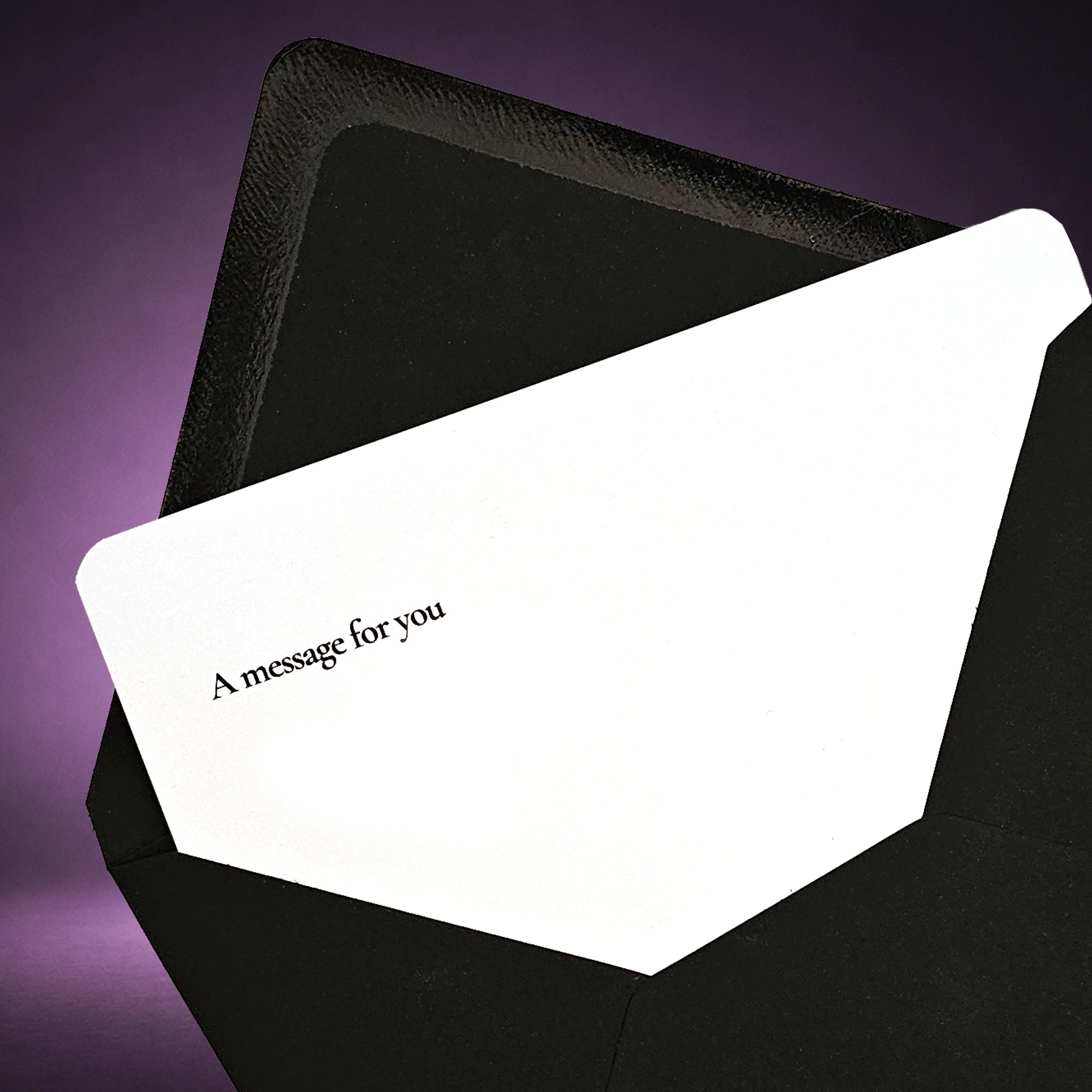 A white greeting card with the printed text 'A message for you' in black, partially tucked inside a black envelope against a dark purple background.