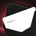 A white greeting card with the printed text 'A message for you' in black, partially tucked inside a black envelope against a dark pink gradient background.