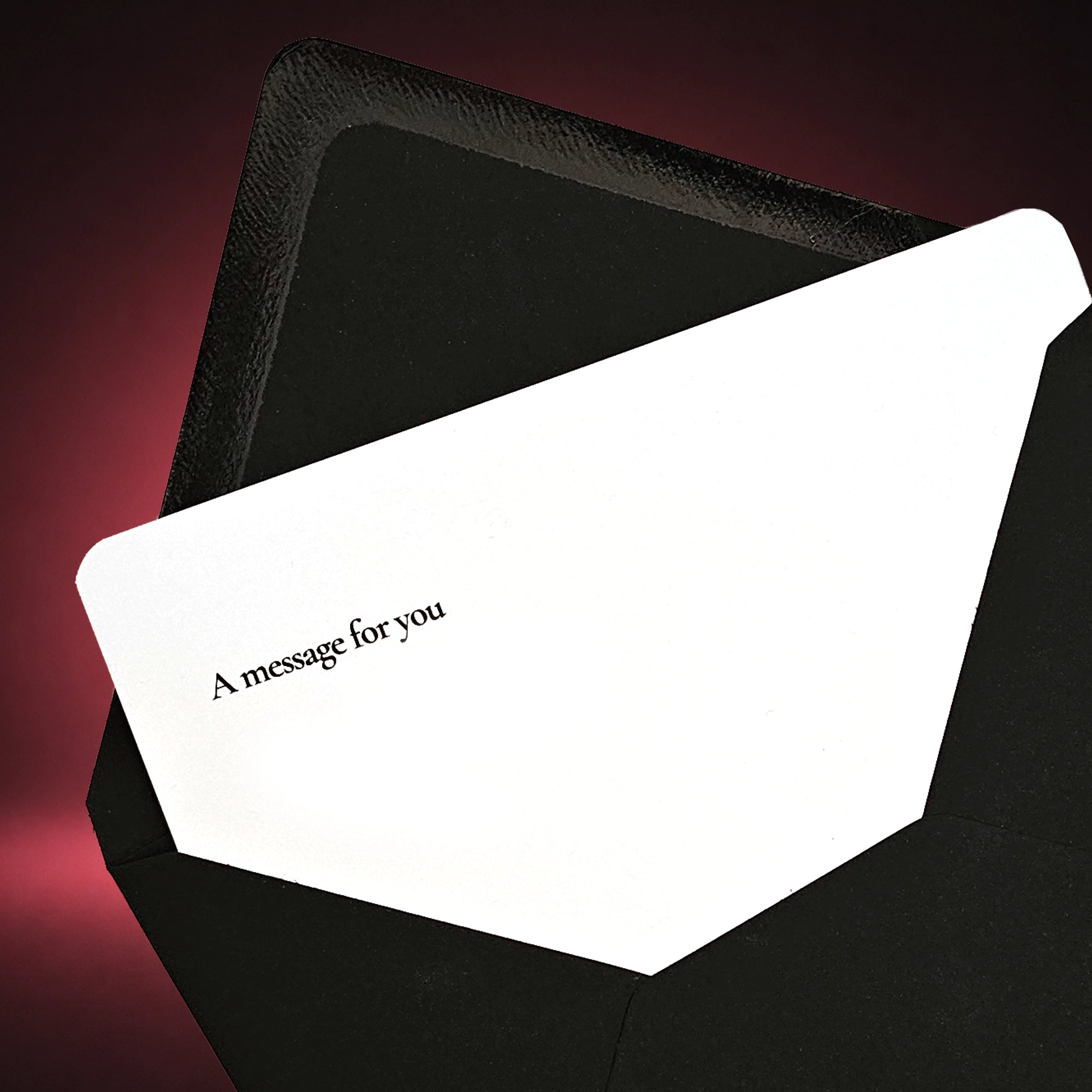 A white greeting card with the printed text 'A message for you' in black, partially tucked inside a black envelope against a dark pink gradient background.