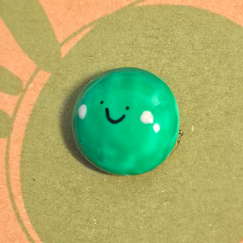 Close-up of Pea of Positivity mindfulness pebble with smiling green pea on cheerful affirmation card.