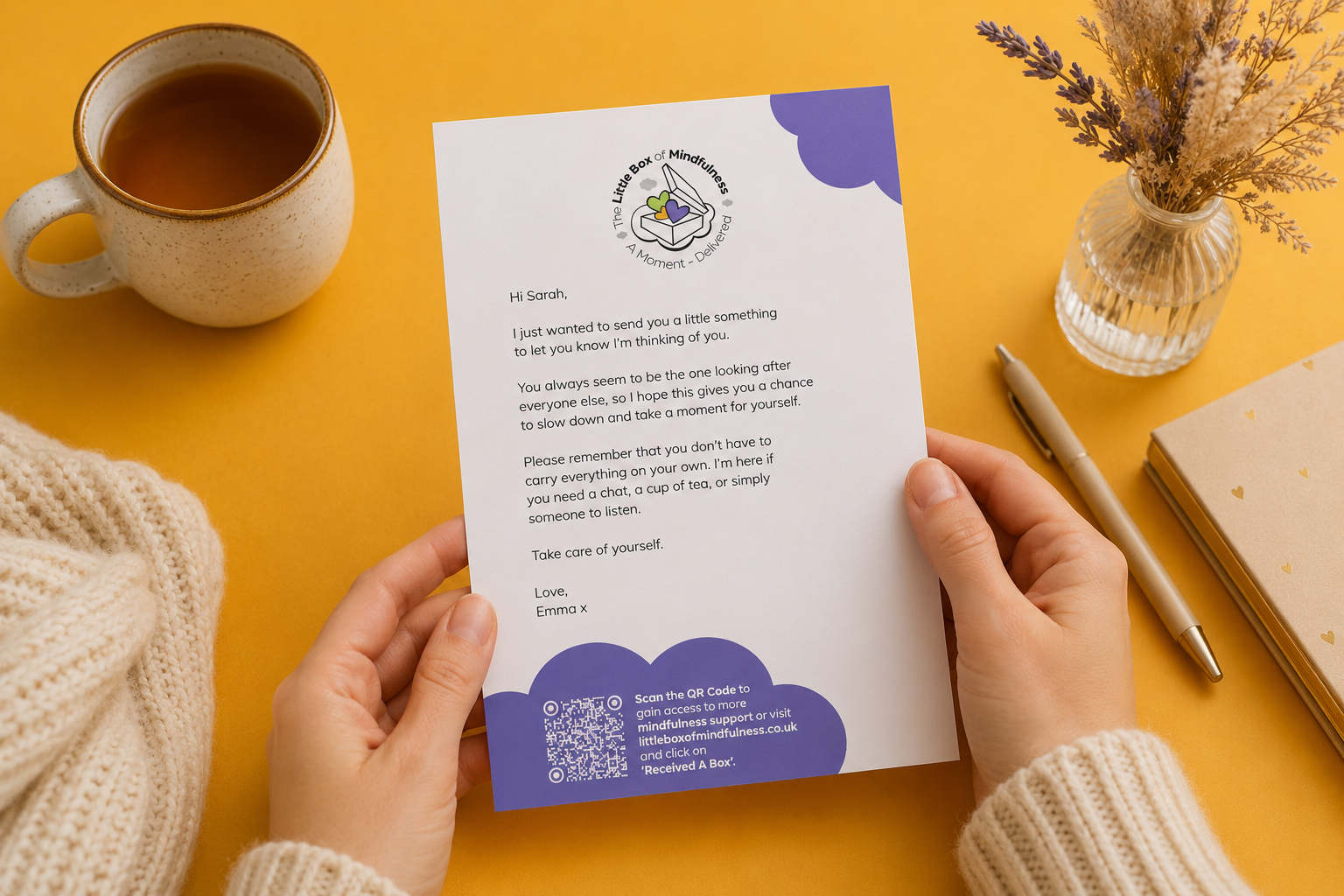 Person holding a letter with a QR code on a yellow background with a cup of tea and vase.