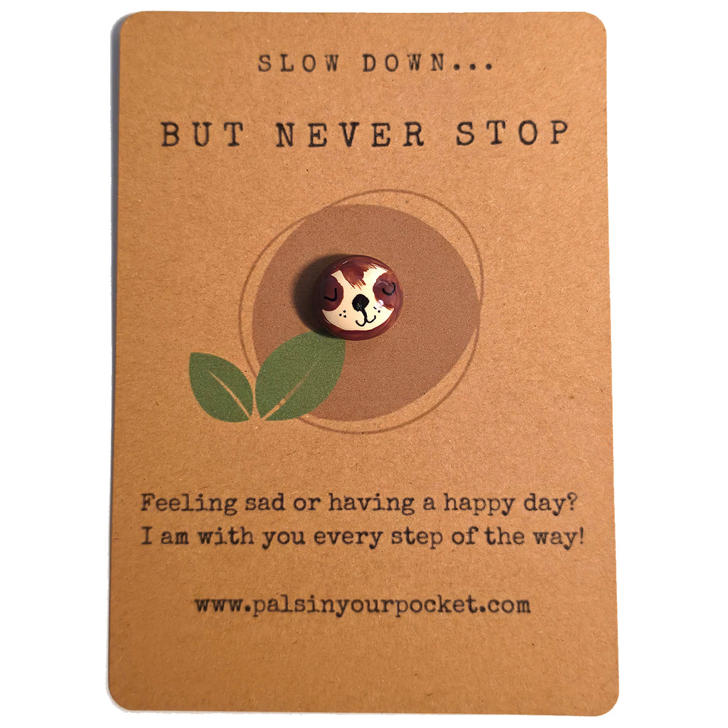 Slow Down But Never Stop mindfulness pebble with cute sloth face on motivational affirmation card.