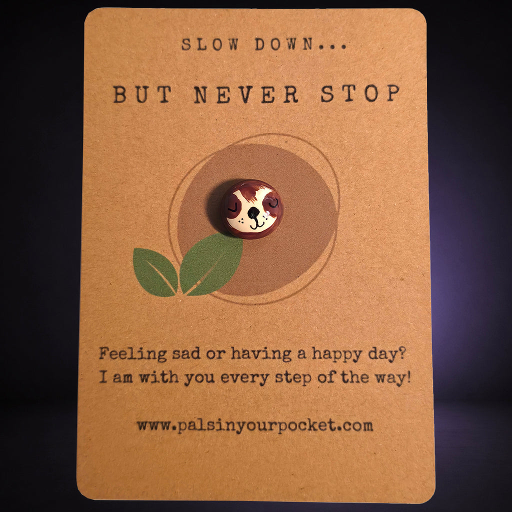 Slow Down But Never Stop mindfulness pebble with cute sloth face on motivational affirmation card.