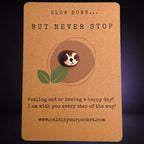 Slow Down But Never Stop mindfulness pebble with cute sloth face on motivational affirmation card.