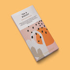 A chocolate bar package labelled 'TEA & BISCUIT' by The Chocolate Society, shown at an angle on a solid warm peach background. The box is mostly white with abstract blush pink, orange, gray, and black shapes, plus small text describing blend 6 dark chocolate.