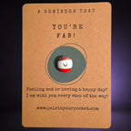 A Reminder That You're Fab mindfulness pebble with smiling face on uplifting affirmation card.
